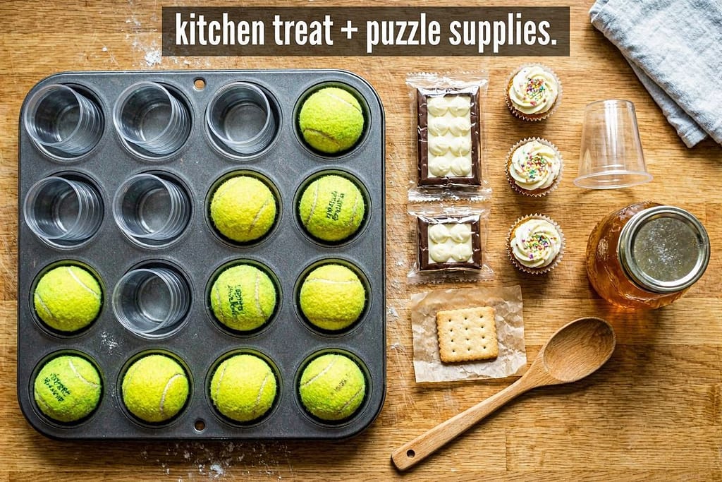 Supply flat lay (Kitchen) Muffin tin, tennis balls, plastic cups, baking sheet, treats. Text: "Kitchen = treat + puzzle supplies."